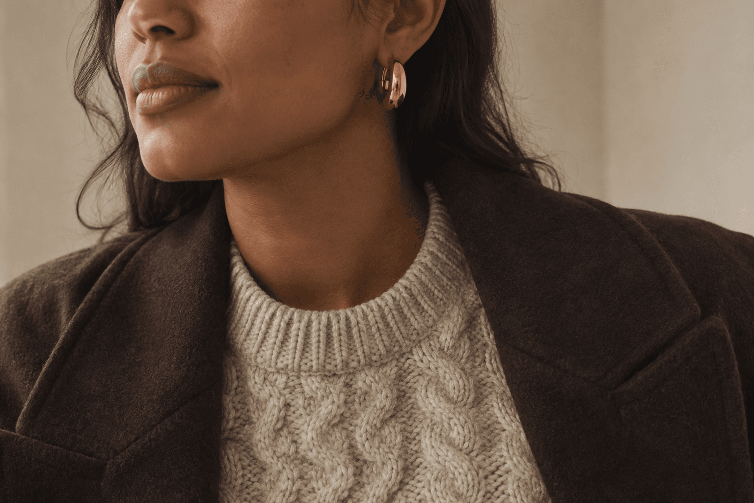 A gold hoop worn with an oatmeal cable-knit sweater and an open brown wool jacket